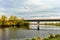 An automobile bridge over a small river surrounded by cottages and farm fields