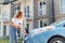 Automobile is charging. Young woman in casual clothes with her electromobile outdoors at daytime