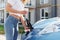 Automobile is charging. Young woman in casual clothes with her electromobile outdoors at daytime