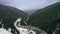 Automobile road between the mountains covered with forest. Dark winter evening with clouds.