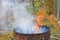 Autumn activity in garden, burning leaves, branches and dry grass in a old rusty barrel. Air pollution from farmers in the