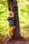 Autumn baby boy stands near a tree, looking back forest