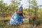 Autumn berries picking: young woman on swamp searching for ripe cranberry spend weekend outside city