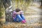 In the autumn birch forest  a little sad upset girl sits under a tree near the path