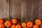 Autumn bottom border of pumpkins and fall leaves, top view over a rustic wood background