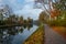 Autumn Canal Tranquility: Trees, Leaves, and Cloudy Reflections