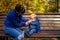 Autumn cold in children - concept. a young mother in blue clothes on a park bench wipes the nose of little baby who has