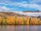 Autumn coloured trees on the lakeside with blue sky and low laying white cloud