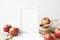 Autumn composition of white 5x7 blank frame mockup on white wall background with red apples, cinnamon, white candle and dried flow