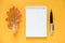 Autumn composition. White blank notepad, dried orange oak leaf and pen on yellow background. Top view Flat lay Mockup Template for