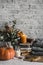 Autumn cozy home still life. Pumpkin, stack of books, burning candle, pile of winter autumn sweaters, jar of marshmallows on the