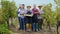 In the autumn day group of farmers posing in front of the camera in the middle of vineyard they smiling large holding