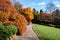 Autumn fall golden leaves in orange, yellow and red in garden setting with winding pathway around green grass