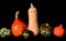 In autumn, a family of brightly colored, different ornamental gourds stands side by side against a dark background with shiny eyes