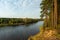 Autumn forest along the river and lake. The setting sun illuminates the treetops. Steep steep sandy bank above a wide river.