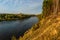 Autumn forest along the river and lake. The setting sun illuminates the treetops. Steep steep sandy bank above a wide river.