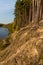 Autumn forest along the river and lake. The setting sun illuminates the treetops. Steep steep sandy bank above a wide river.