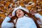 Autumn girl playing in city park. Portrait of an autumn woman lying over leaves and smiling outside in fall forest. Beautiful ener