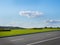 Autumn landscape with asphalt road, green lawn under sky with clouds