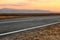 Autumn landscape with an asphalt road and spectacular sunset above mountains on horizon