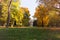 Autumn landscape city park, Gothic architectural fragment of historic tower in the middle, green grass with autumn leaves and colo