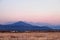 Autumn landscape with snowy mountains behind field covered with dry yellow grass during spectacular colorful sunset