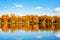 Autumn landscape, yellow leaves trees on river bank on blue sky and white clouds background on sunny day, reflection in water