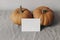 Autumn mockup. Closeup of blank greeting card, invitation with orange pumpkins on beige linen table cloth. Blurred white