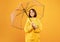 Autumn mood. Portrait of pretty young woman standing under umbrella and smiling, posing over yellow background