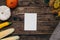 Autumn mood: white empty present card , pumpkins and corn with yellow leaves on a wooden background