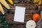 Autumn mood: white notebook, pumpkins and corn with yellow leaves on a wooden background