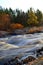 Autumn morning in Koiteli rapid, Kiiminki river. Rising sun, bright light. Flowing blue water, rocks along the river. Autumn color