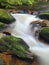 Autumn mountain river with blurred waves, water is running between mossy boulders and bubbles create trails on level.