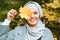 Autumn muslim woman holding maple leaf outdoors in sunny day. Beautiful arab wearing hijab girl in fall park