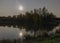 Autumn night landscape with a lake in the moonlight, trees and the moon in the calm lake water, autumn colors