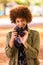 Autumn outdoor portrait of beautiful African American young woman holding a digital camera - Black people