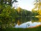 Autumn park landscape with people boating in a lake and the green foliage of the trees start to turn yellow