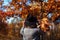 Autumn season. Young woman walking in fall park admiring nature and holding bouquet of leaves