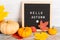 Autumn still life image with pumpkins, colorful maple foliage and letter board with words Hello Autumn against white wooden wall