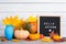 Autumn still life image with pumpkins, vase with colorful maple foliage and letter boards with words Hello Autumn against white
