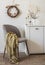 Autumn style interior. An armchair with a plaid, a chest of drawers with autumn decor, a homemade autumn wreath on the wall in the