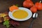 Autumnal pumpkin soup in a bowl with hokkaido pumpkins, leaves and a spoon on a brown wooden table