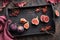 Autumntime background. Fresh halved fig fruits on black wooden tray. Magenta towel and dry red Autumn leaves on dark
