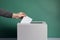 average citizen hand casting a vote paper election ballot in a voting box on a geen background. Caucasian man putting a balloting