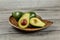 Avocado cut in half, seed and pulp visible, two more whole pears on carved wooden bowl