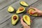 Avocado halves on gray desk, woman hands with red nails hold two of them