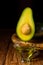 Avocado oil drops drain into a glass bowl. Avocado fruit and avocado oil on a wooden rustic tray on table