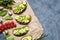 Avocado summer sandwich toast recipe with guacamole, spinach, arugula and quail eggs on parchment paper on a concrete