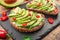 Avocado toasts - bread with avocado slices, pieces of red pepper and sesame on black stone board