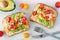 Avocado toasts with hummus and tomatoes, overhead on marble